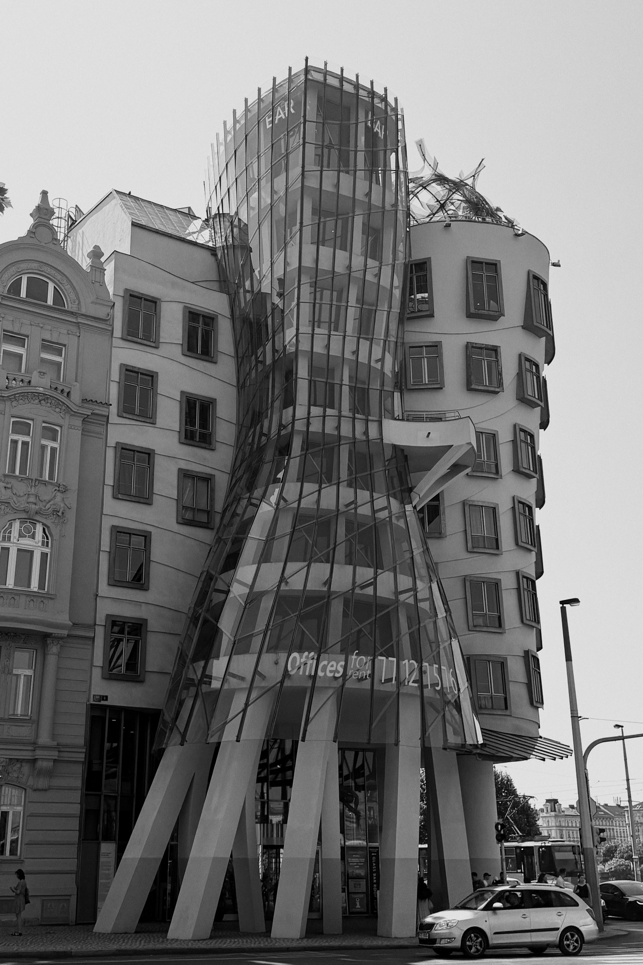The Dancing House, Prague: a glass tower pinched at the waist and leaning against a solid stone tower, seen from street level.